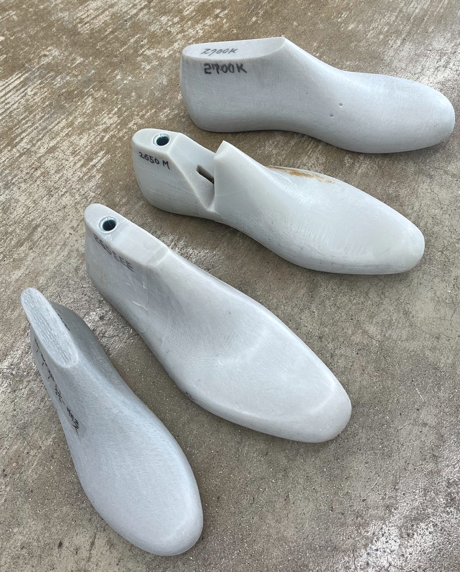 A row of shoe lasts on a concrete floor, each hand-marked with its size and width code